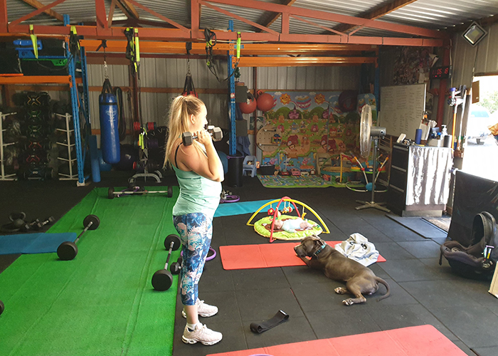 A woman lifting weights in the Back to Basics 4 Life Fitness Studio with dog by her side - pets welcome!